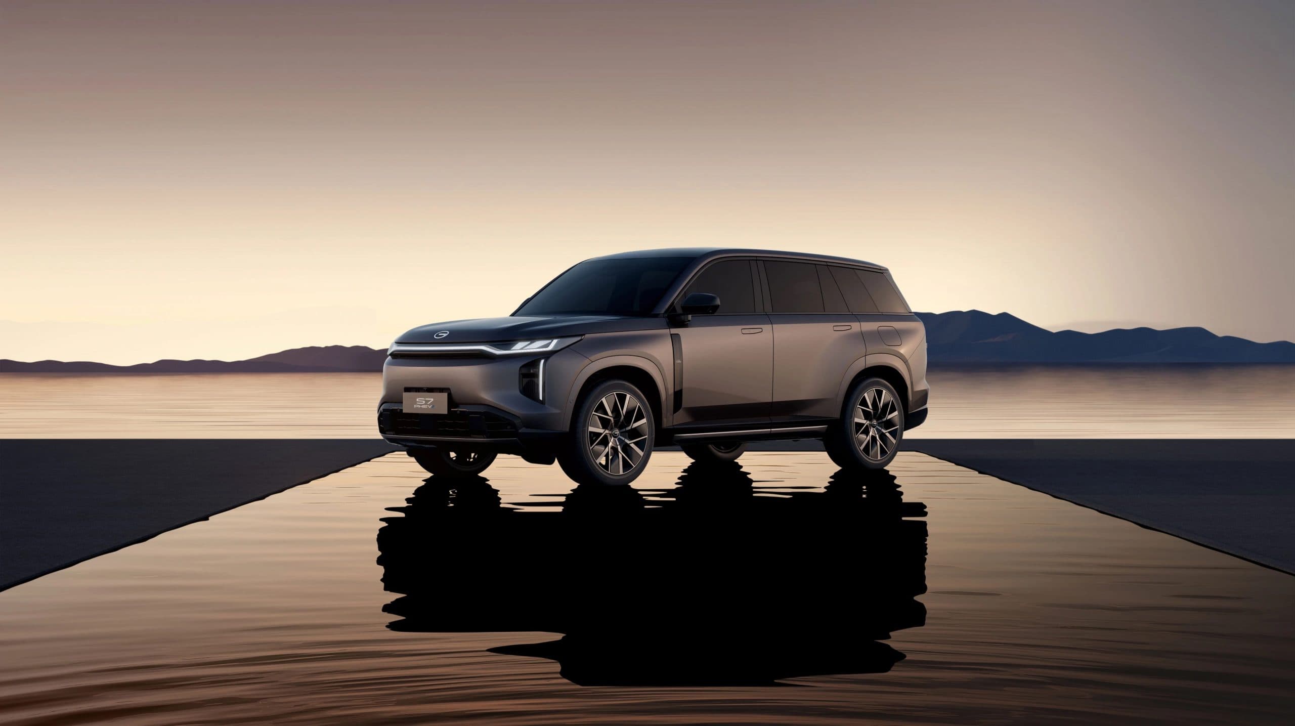 Grey GAC S7 plug-in hybrid SUV parked on a reflective platform at dusk, mountains across the water, S7 PHEV plate