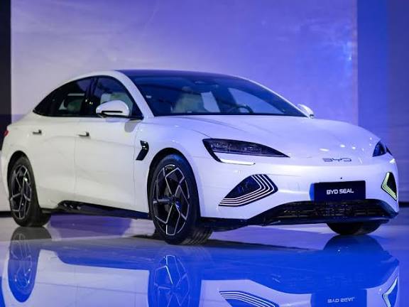 White BYD Seal electric sedan in a showroom with illuminated blue-purple background and glossy floor reflection.
