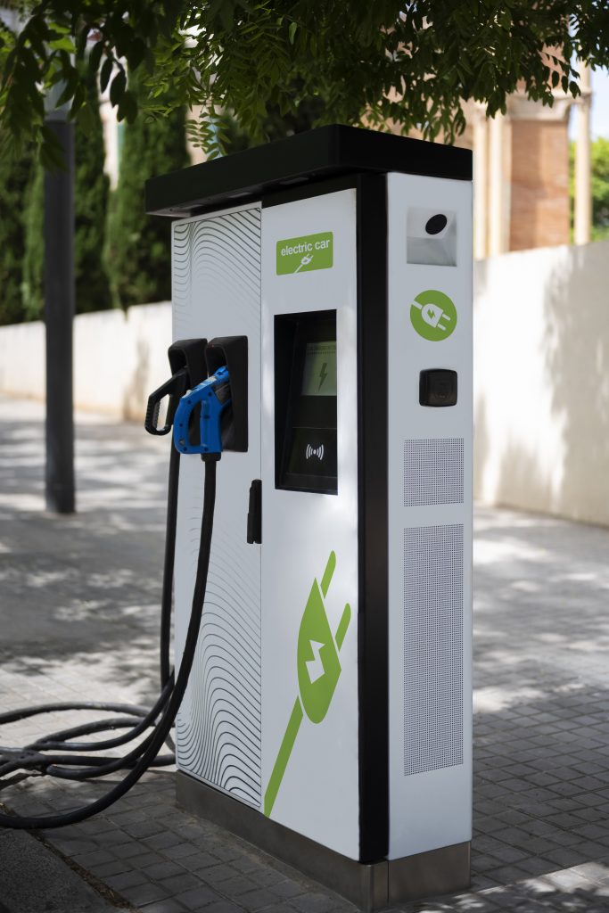 Public electric‑car charging station with multiple charging units and parked EVs in a modern urban setting.