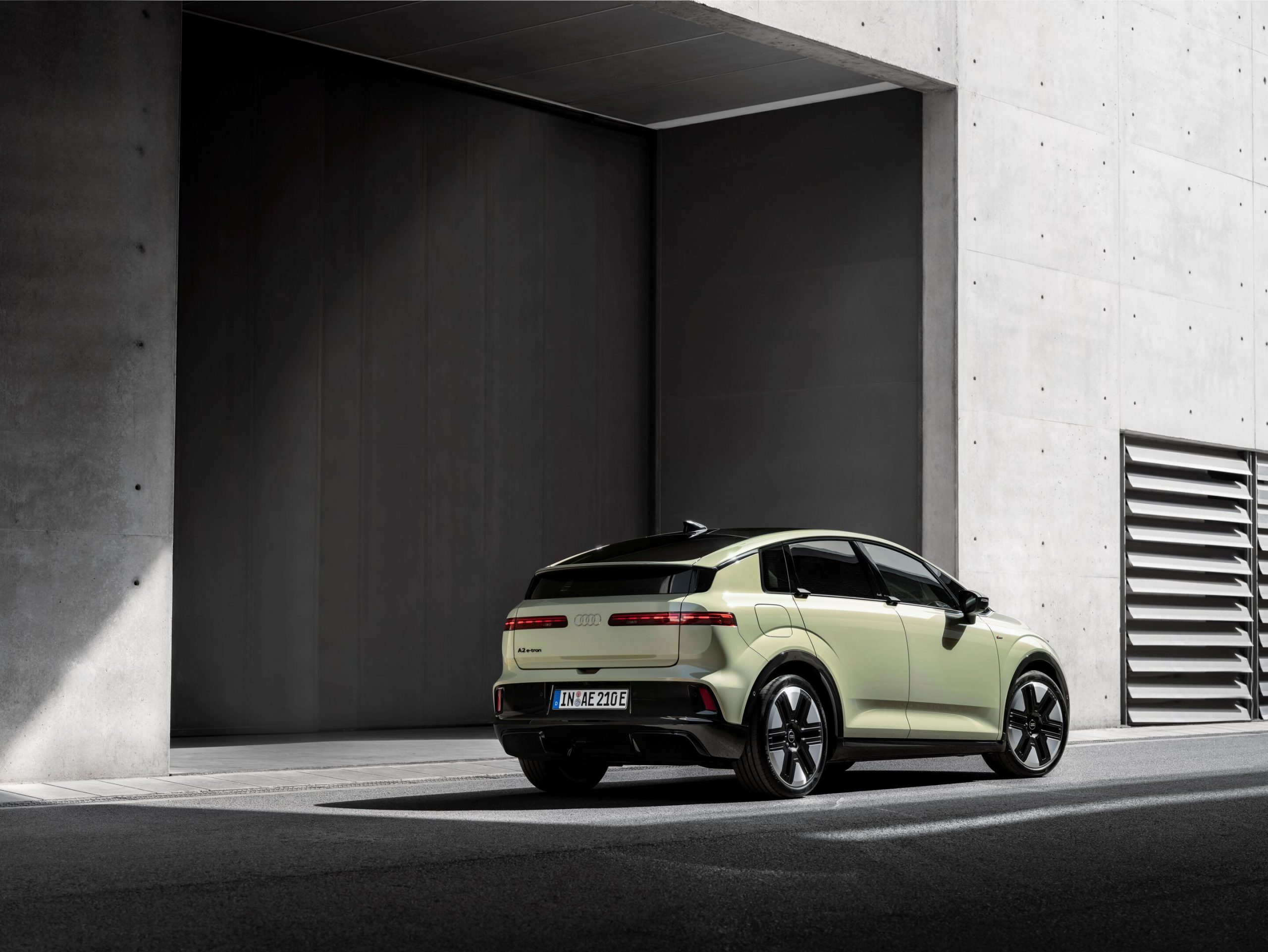Pale green Audi A2 e-tron compact electric hatchback, rear three-quarter view, German IN AE 210 E plates, parked in front of a concrete building