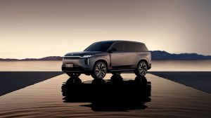 Grey GAC S7 plug-in hybrid SUV parked on a reflective platform at dusk, mountains across the water, S7 PHEV plate