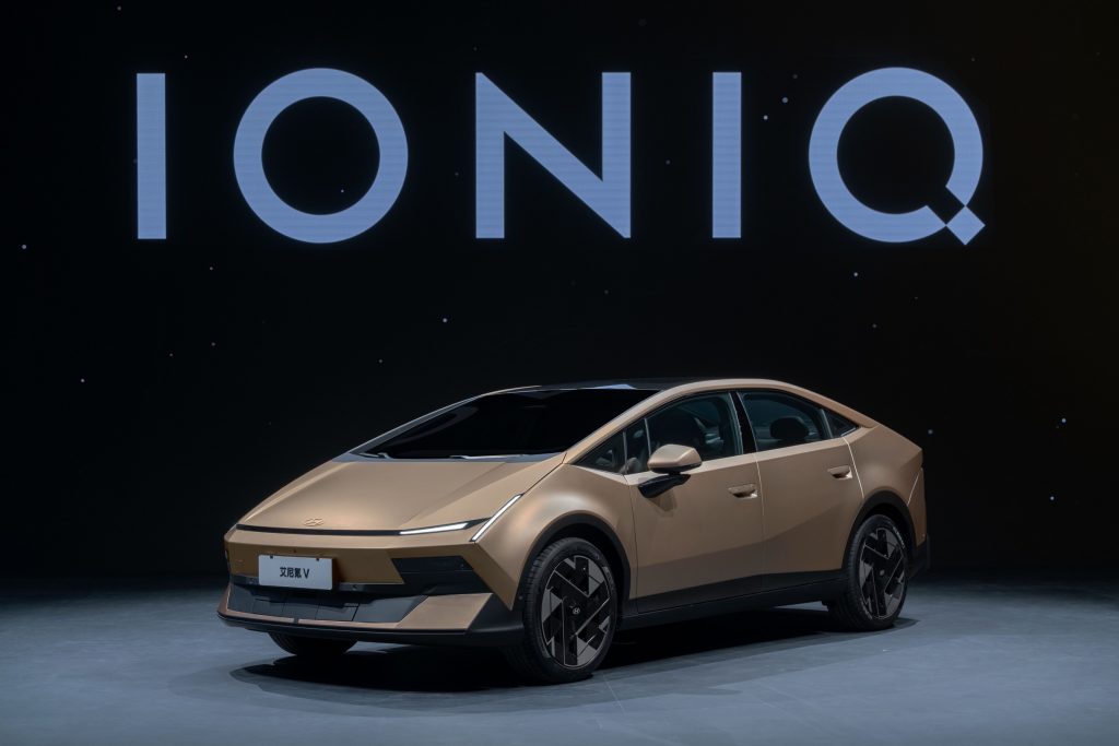 Gold Hyundai Ioniq V fastback sedan on a studio floor under an IONIQ backdrop