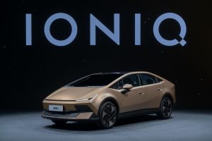 Gold Hyundai Ioniq V fastback sedan on a studio floor under an IONIQ backdrop