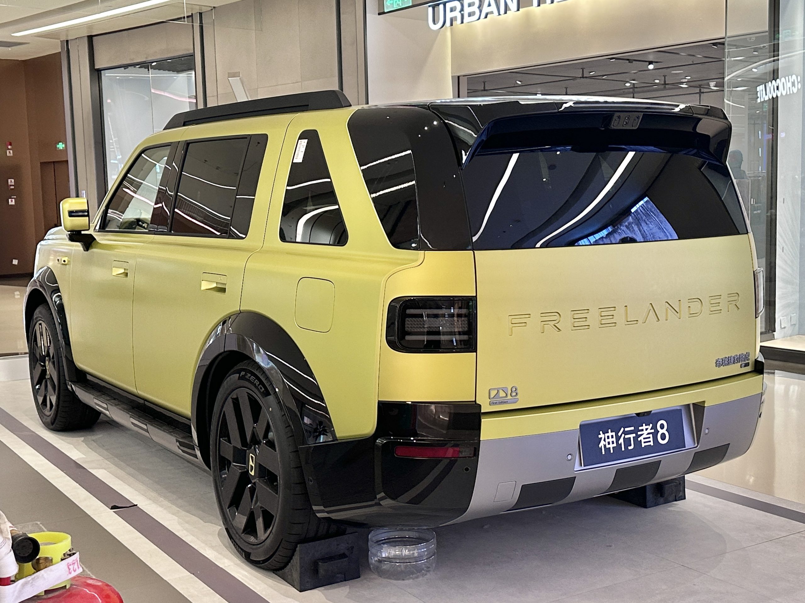 Rear three-quarter of a pale yellow Freelander 8 on a showroom stand, FREELANDER lettering on the tailgate