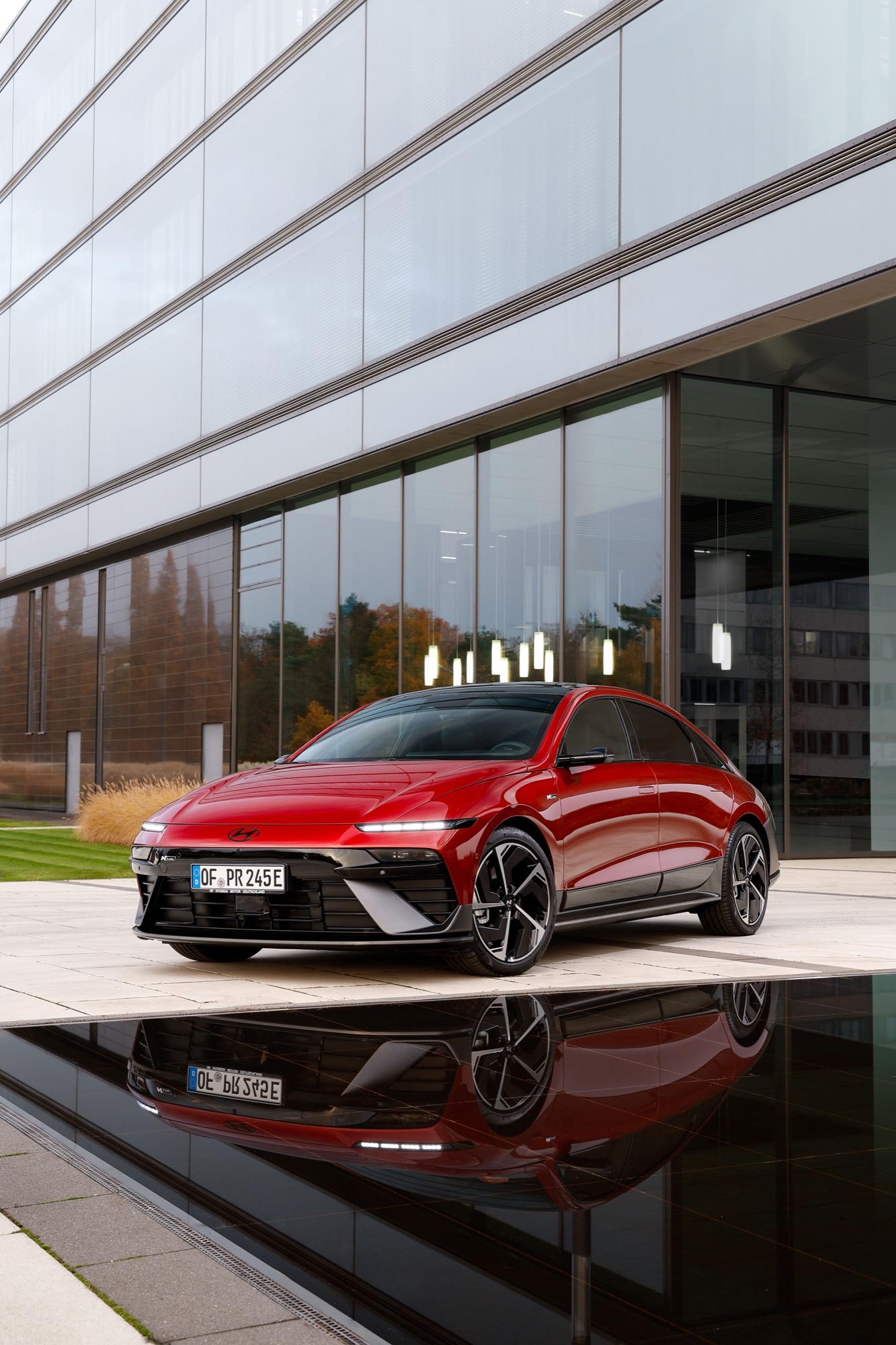 Red Hyundai IONIQ 6 N Line parked beside a glass building, front three-quarter view