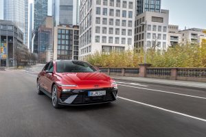 Red Hyundai IONIQ 6 N Line in Ultimate Red, driving on a city road, front three-quarter view